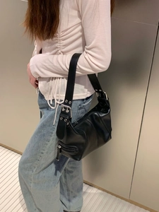 Detail of a black leather underarm bag with silver buckles worn by a model in casual wear