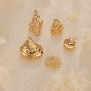 Five golden bohemian shell pendants with intricate cutout design on beige silk backdrop