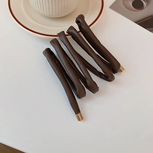 Detail of coffee brown lychee pattern leather hair tie with gold metal ends on white desk