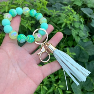 Mint green silicone beaded keychain bracelet with tassels held against natural green leaves