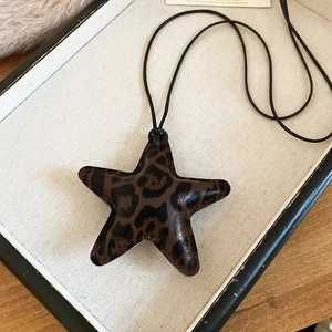 Close-up of leopard print star pendant on a black leather cord necklace over fabric