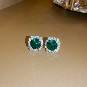 Makroaufnahme von smaragdgrünen Ohrringen mit Diamantkranz und goldenem Hintergrund