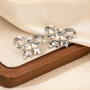 Detailed view of silver bow-shaped stud earrings on a dark wood jewelry tray