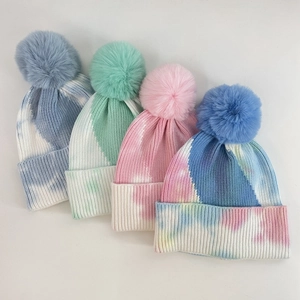 Flat lay of colorful tie-dye knit beanies with fluffy faux fur pom poms for winter
