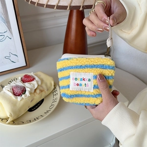 Detailed close-up of a striped plush mini makeup bag with zipper and hand strap