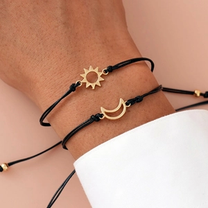 Close-up of handmade sun and moon charm bracelets worn on wrist with adjustable black cord