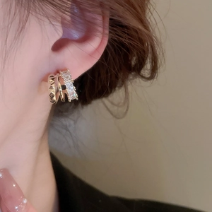 Detail shot of three-layer gold C-shaped earrings with cubic zirconia and metal studs