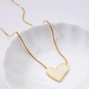 Detailed close-up of a gold heart pendant necklace with white shell inlay on a white plate