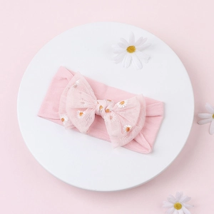 Detail of pink embroidered daisy flower mesh bow headband for babies on a white circular plate