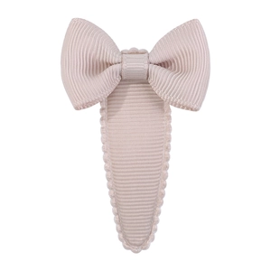 Detail of a beige ribbed fabric bow hair clip with decorative wavy scalloped edges