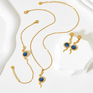 Detailed close-up of golden snake jewelry set with blue oval gemstones on white marble