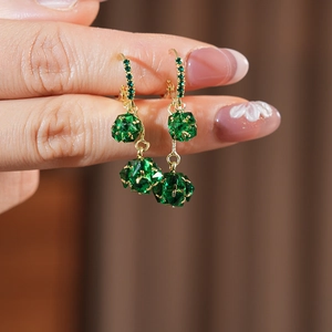 Detail showing gold earrings with green rhinestones and faceted spherical pendants