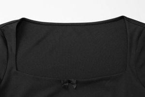 Détail du col en U d'une robe noire avec un petit nœud décoratif et une texture maille fine
