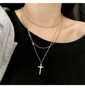 Detail of a triple-layered gold titanium cross necklace on a model with a black top