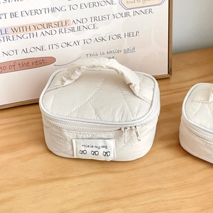 Close-up of a quilted cream makeup bag with top handle and bow detail on a wood surface