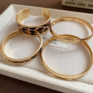Detail of gold bangle set featuring one wide leopard print cuff and three thin gold rings