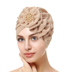 Detail of beige pleated turban cap featuring intricate 3D flower and pearl embellishments