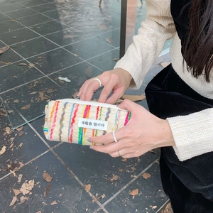 Detail of colorful striped woven makeup bag with fabric label held by a person