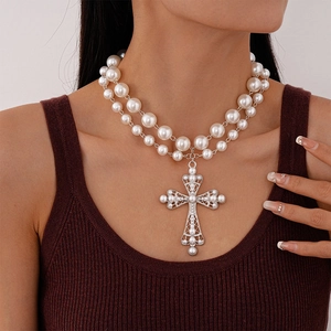 Detail shot of a double-layer pearl necklace with a large hollow cross pendant on a model