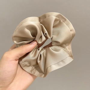 Macro shot of champagne satin scrunchie showing glossy pleated silk texture