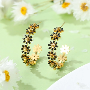 Macro shot of gold C-shaped earrings with black and gold daisy flowers on green background