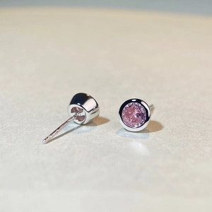 Macro shot showing pink round-cut gemstone and silver bezel setting of stud earrings