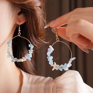 Detail of gold hoop earrings with blue stones and a white starfish charm on a model