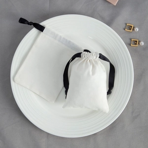 Off-white cotton drawstring pouch for jewelry packaging with black ribbon on a white tray