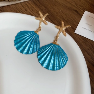 Detailed close-up of golden starfish and blue shell earrings on a ceramic display
