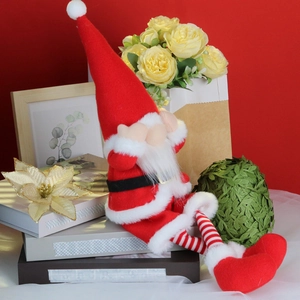 Nordic plush Christmas gnome decoration with long legs sitting on books in festive red setting