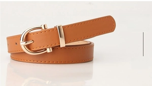 Detail of slim brown PU leather belt with gold horseshoe buckle on white surface