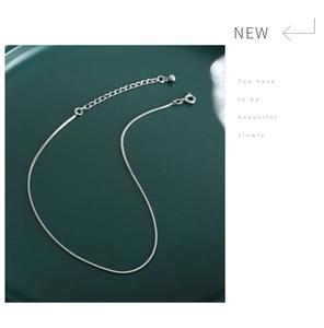 Macro detail of a minimalist silver snake chain anklet displayed on a green jewelry tray