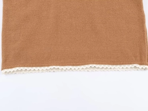 Détail d'un pull en maille marron avec une bordure en dentelle blanche au bas