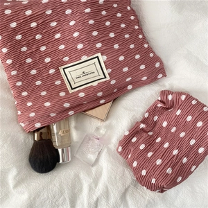 Detail of ruched polka dot makeup bag and matching hair scrunchie set on white texture
