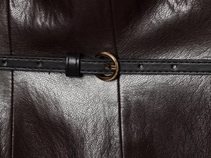 Dettaglio gonna in similpelle marrone scuro con cintura nera e fibbia tonda oro