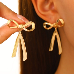 Elegant gold bow earrings with long tassel pendants worn by a model in close-up view