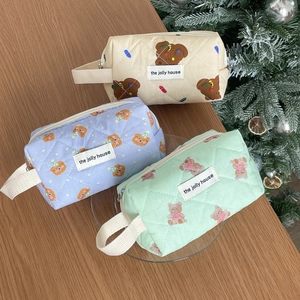 Quilted cartoon bear cosmetic bags in cream, blue, and green on a wooden tabletop