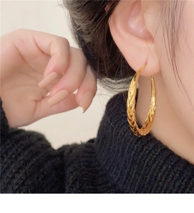 Detail view of large gold twisted hoop earring on model wearing black turtleneck