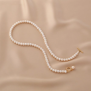 Minimalist freshwater pearl necklace with golden OT toggle clasp on beige silk background