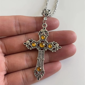 Detail of silver filigree cross pendant with five amber gemstones held by hand