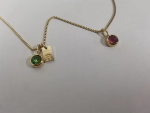 Détail du collier boîte doré avec pendentif B et breloques de pierres rouge vert