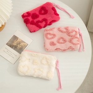 Three colors of plush makeup bags with 3D heart patterns and zipper closure on a white table