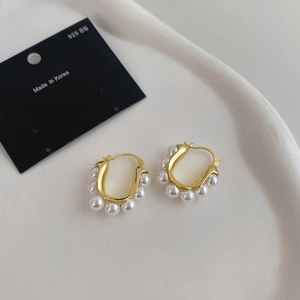Close-up of U-shaped gold earrings with white pearls on a minimalist ceramic plate