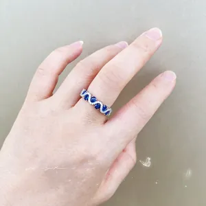 Close-up of wavy band ring with five oval blue gemstones and pavé diamonds on hand