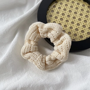 Detail of beige ribbed knit scrunchie texture on a black woven coaster and white fabric