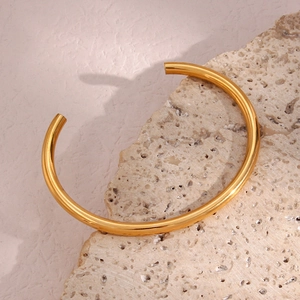 Detailed view of polished 18K gold plated minimalist open bangle on a natural stone base