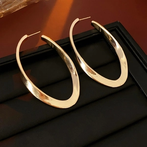 Close-up of golden twisted oval earrings resting on a textured black jewelry tray