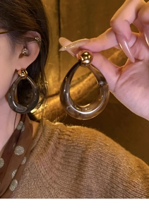Close-up of tortoise shell resin teardrop earrings with golden sphere studs and metal details