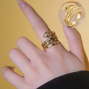 Layered gold snake ring with green zircon eyes and clear crystals in an open design