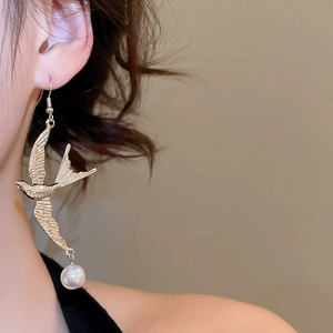 Detailaufnahme von goldenen Schwalbenohrringen mit Perlenanhängern an einem Model